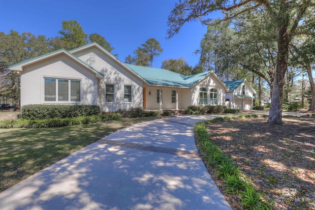 view of front of house with decorative driveway, metal roof, and a front lawn