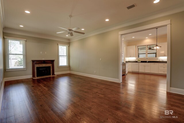 unfurnished living room with plenty of natural light, ornamental molding, dark wood finished floors, and a high end fireplace