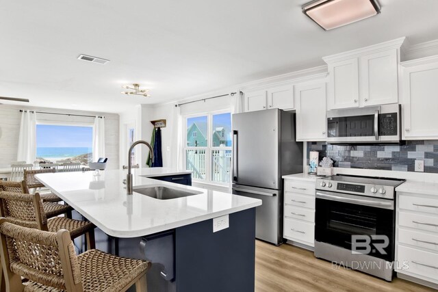 kitchen featuring white cabinetry, a kitchen island with sink, stainless steel appliances, and a kitchen bar