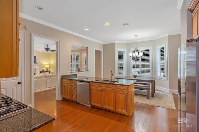 kitchen featuring dark stone counters, appliances with stainless steel finishes, light wood-type flooring, pendant lighting, and ceiling fan with notable chandelier