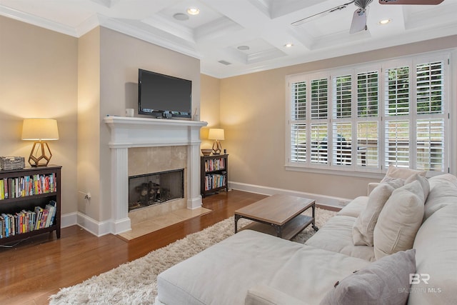 living room featuring crown molding, ceiling fan, coffered ceiling, hardwood / wood-style flooring, and a tiled fireplace