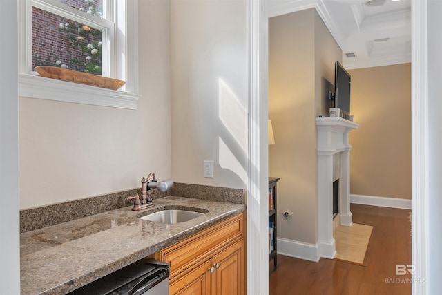 kitchen with ornamental molding, sink, dark wood-type flooring, and dark stone countertops