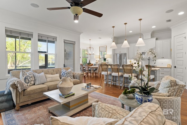 living area featuring ceiling fan with notable chandelier, wood finished floors, crown molding, and visible vents
