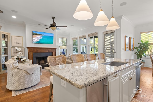 kitchen with open floor plan, ornamental molding, a sink, light wood-style floors, and a kitchen island with sink