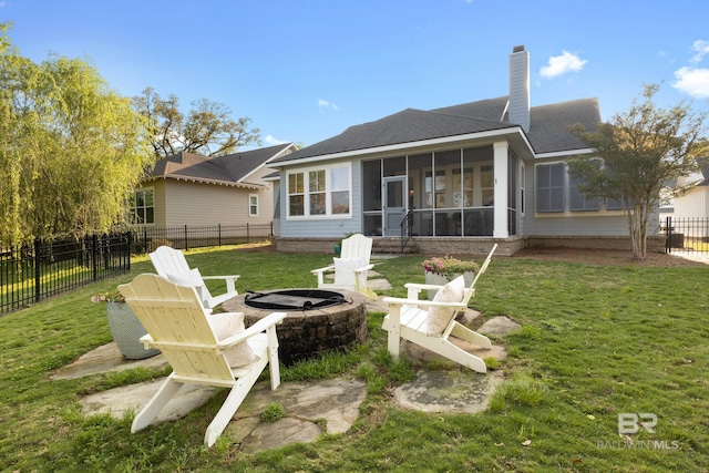 rear view of property with a sunroom, a lawn, a fenced backyard, an outdoor fire pit, and a chimney