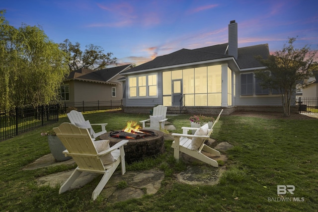 back of house featuring an outdoor fire pit, a chimney, a sunroom, fence private yard, and a lawn