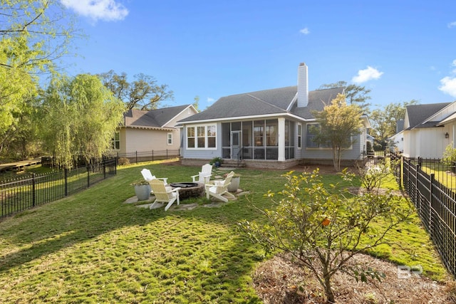 back of property featuring a sunroom, a fenced backyard, a lawn, a shingled roof, and a fire pit