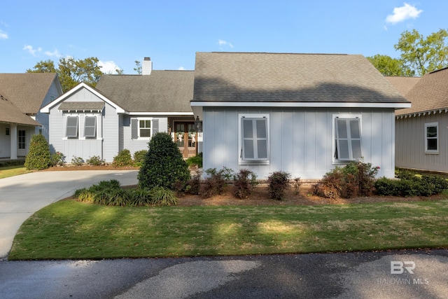 ranch-style home with roof with shingles, board and batten siding, driveway, a front yard, and a chimney