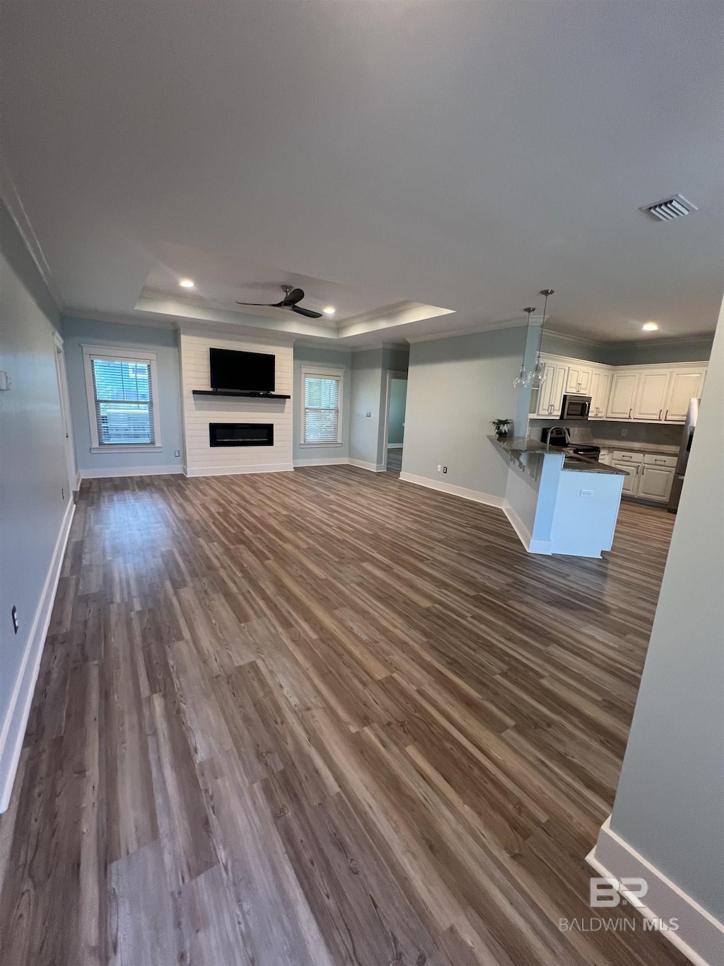 1244 Dorado Way, Gulf Shores, AL 36542 - unfurnished living room featuring baseboards, a raised ceiling, dark wood-style flooring, recessed lighting, and crown molding