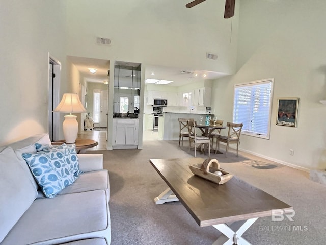 living area with a towering ceiling, baseboards, light carpet, and visible vents