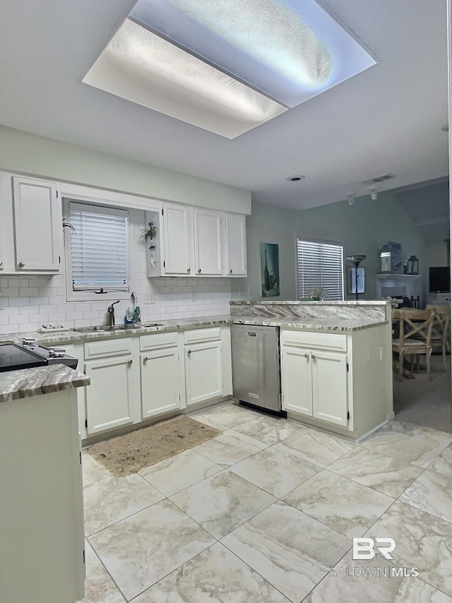 kitchen featuring tasteful backsplash, stainless steel dishwasher, white cabinets, a sink, and a peninsula