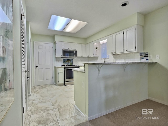 kitchen featuring a breakfast bar, marble finish floor, appliances with stainless steel finishes, white cabinetry, and a peninsula