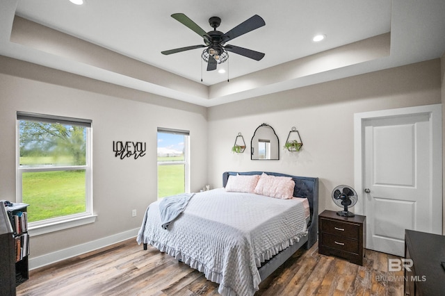 bedroom featuring recessed lighting, a tray ceiling, baseboards, and dark wood finished floors