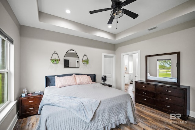 bedroom with dark wood-type flooring, a tray ceiling, visible vents, and recessed lighting