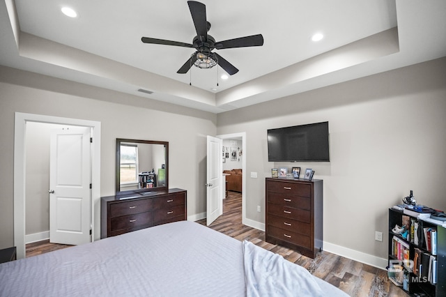 bedroom featuring dark wood-style flooring, a tray ceiling, baseboards, and visible vents