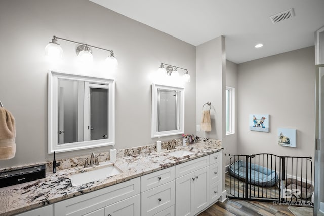 bathroom with visible vents, a sink, double vanity, and wood finished floors
