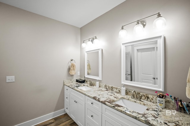 bathroom with baseboards, double vanity, a sink, and wood finished floors
