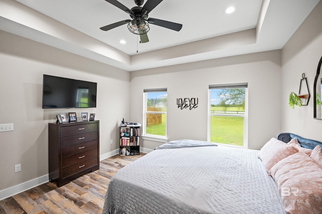bedroom featuring a tray ceiling, baseboards, wood finished floors, and recessed lighting