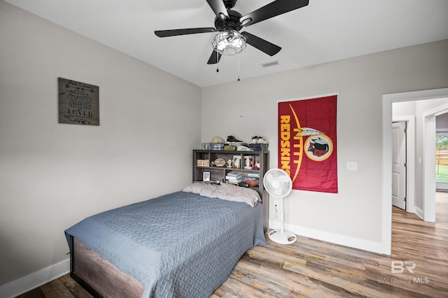 bedroom with a ceiling fan, visible vents, baseboards, and wood finished floors