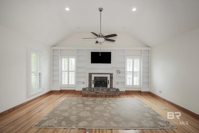 unfurnished living room featuring vaulted ceiling, a healthy amount of sunlight, a fireplace, and light hardwood / wood-style floors