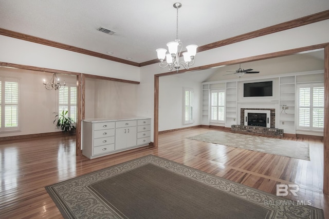 unfurnished living room with hardwood / wood-style floors, ornamental molding, a brick fireplace, built in shelves, and vaulted ceiling