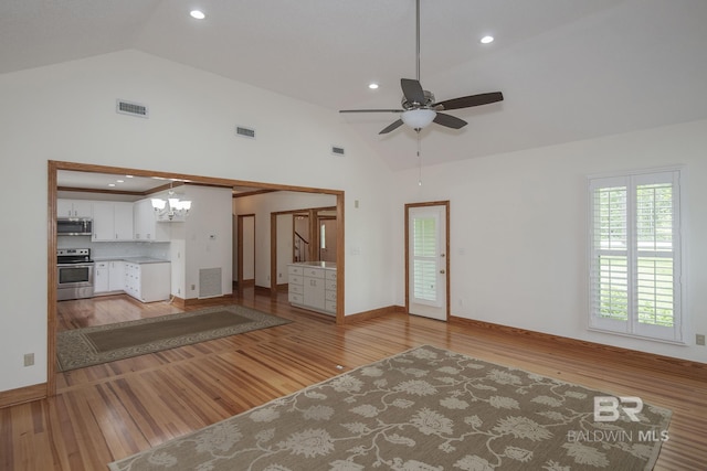 unfurnished living room with ceiling fan with notable chandelier, high vaulted ceiling, and light hardwood / wood-style floors