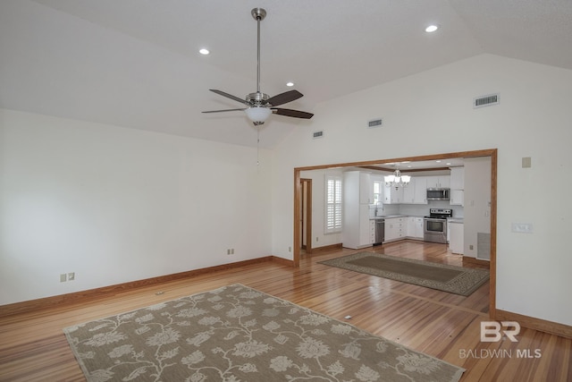 unfurnished living room featuring sink, ceiling fan with notable chandelier, light hardwood / wood-style floors, and high vaulted ceiling