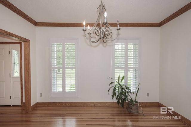 unfurnished dining area featuring wood-type flooring, ornamental molding, and a notable chandelier