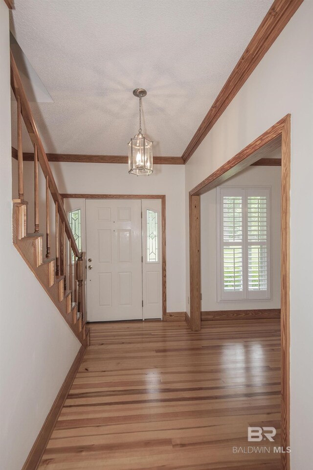 foyer entrance with wood-type flooring, ornamental molding, and a chandelier