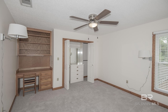 unfurnished bedroom with ceiling fan, light colored carpet, built in desk, and a textured ceiling