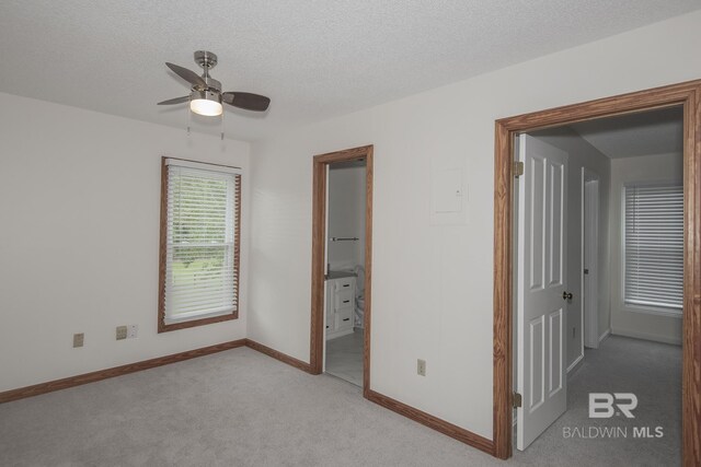 unfurnished bedroom featuring connected bathroom, light colored carpet, a textured ceiling, and ceiling fan