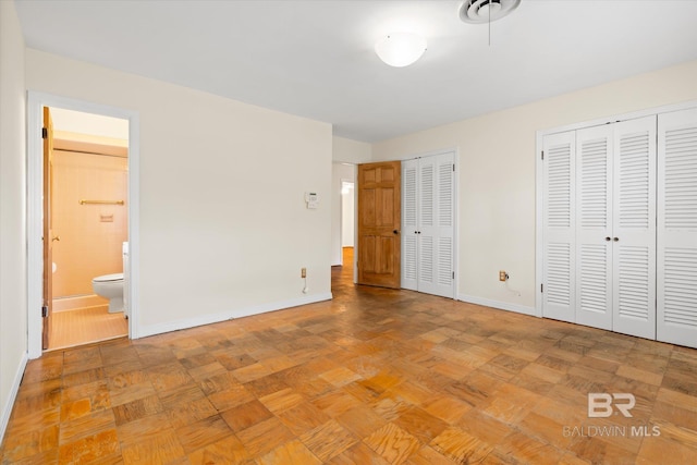 unfurnished bedroom featuring ensuite bathroom, light parquet floors, and two closets