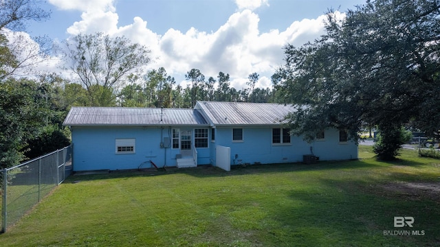 back of property with metal roof, a yard, and fence