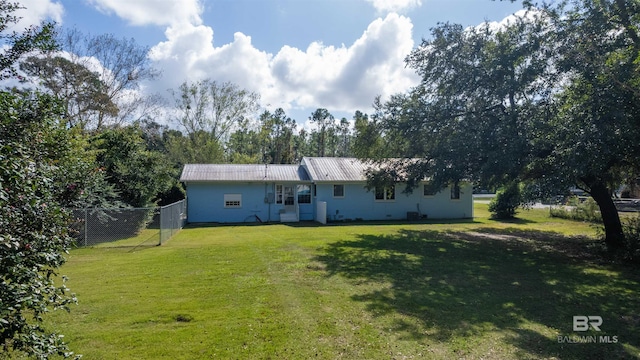 rear view of house featuring fence, metal roof, and a lawn