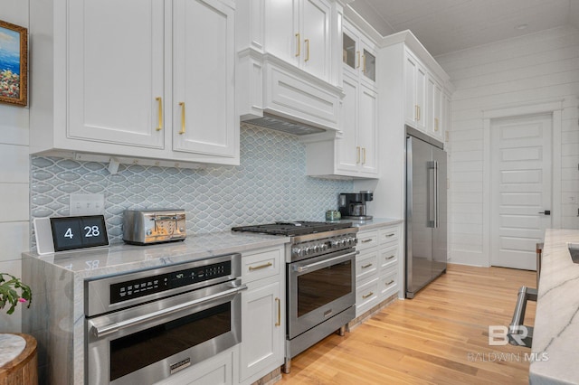 kitchen with high end appliances, backsplash, light wood-style flooring, white cabinets, and light stone countertops