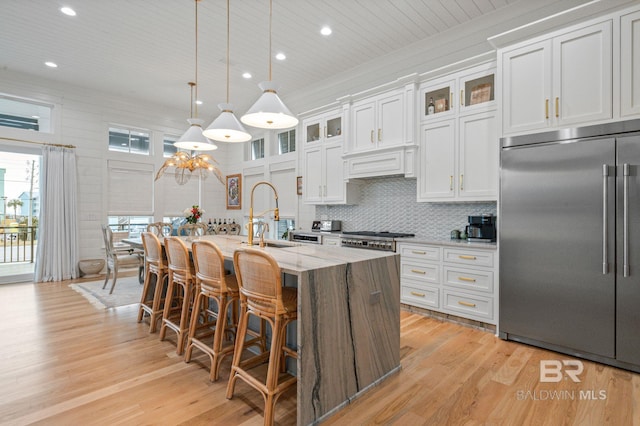 kitchen featuring light wood finished floors, tasteful backsplash, a center island with sink, white cabinets, and stainless steel built in fridge