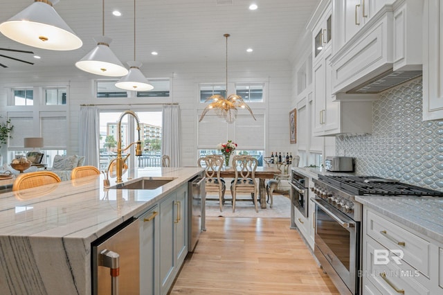 kitchen featuring light wood-style flooring, a sink, high end stainless steel range oven, custom exhaust hood, and an inviting chandelier