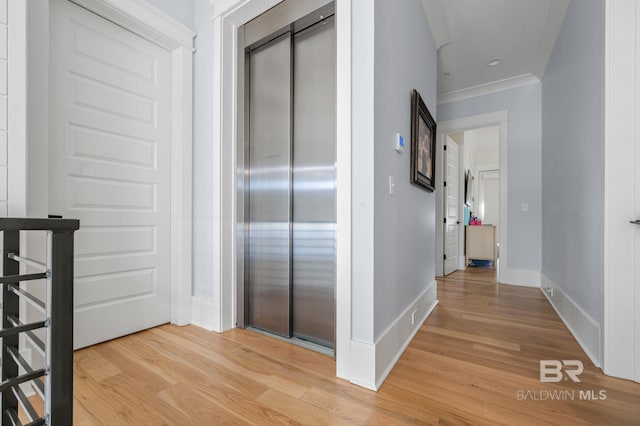 corridor with light wood-style floors, elevator, ornamental molding, and baseboards