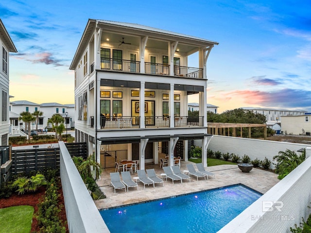 back of property at dusk featuring ceiling fan, a patio area, a fenced backyard, and a balcony