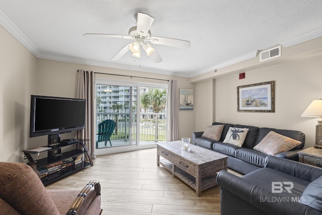 living room with light wood-style floors, a textured ceiling, a ceiling fan, ornamental molding, and visible vents