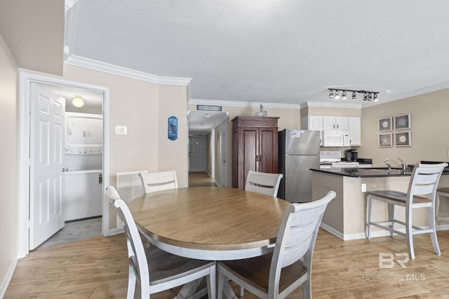 dining area featuring light wood-type flooring, stacked washer and dryer, ornamental molding, and a textured ceiling