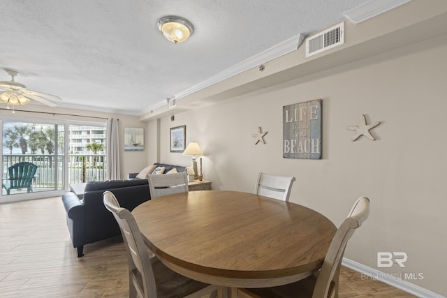 dining area with visible vents, ornamental molding, a ceiling fan, a textured ceiling, and wood finished floors