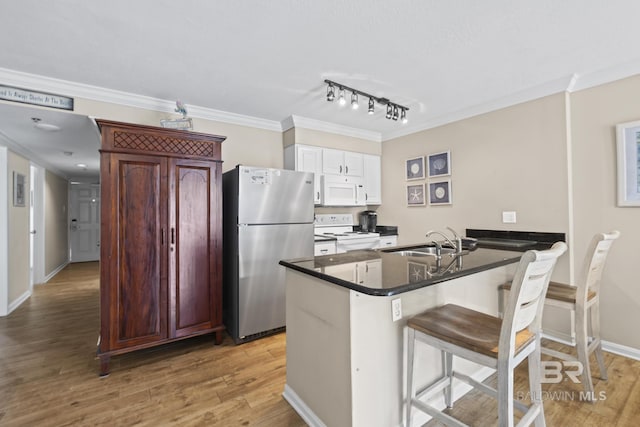 kitchen with a sink, dark countertops, white appliances, and crown molding