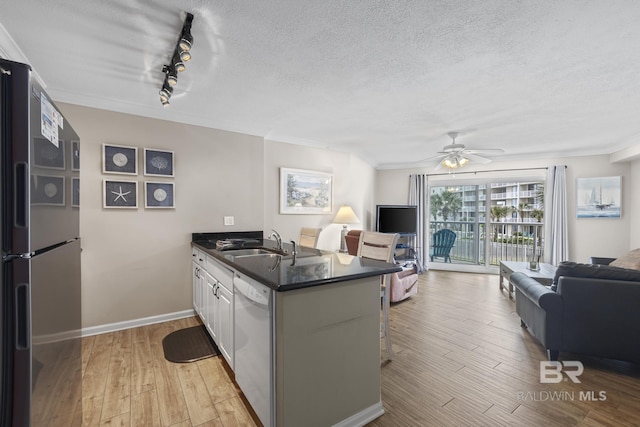 kitchen featuring open floor plan, a peninsula, freestanding refrigerator, white dishwasher, and a sink
