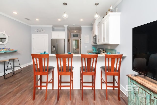 kitchen featuring white cabinetry, a kitchen bar, hanging light fixtures, ornamental molding, and stainless steel appliances