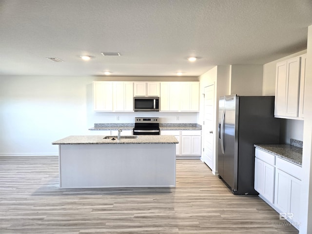 kitchen featuring sink, appliances with stainless steel finishes, a kitchen island with sink, light stone counters, and white cabinets