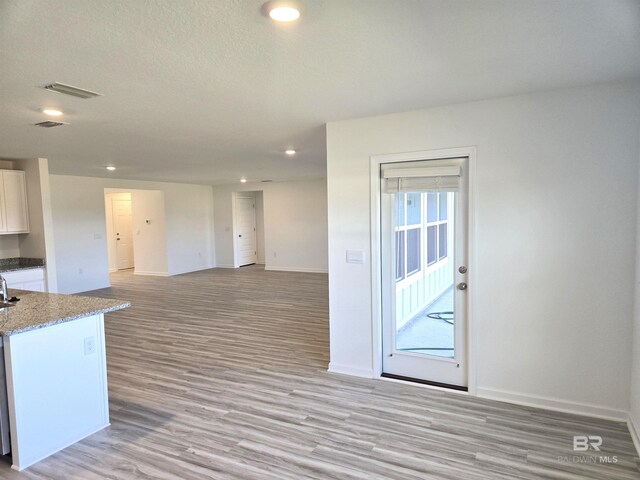 kitchen featuring dishwasher, light wood-type flooring, white cabinets, light stone counters, and a textured ceiling