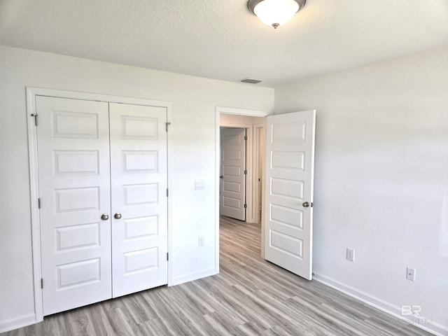 unfurnished bedroom featuring a closet, light hardwood / wood-style flooring, and a textured ceiling