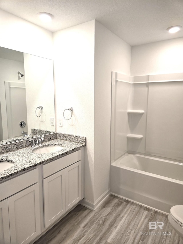 full bathroom with hardwood / wood-style flooring, shower / tub combination, vanity, a textured ceiling, and toilet