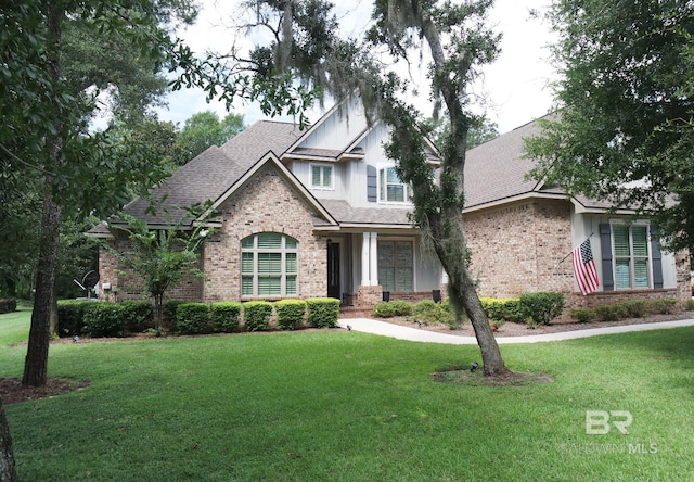 view of front facade featuring a shingled roof, a front yard, and brick siding